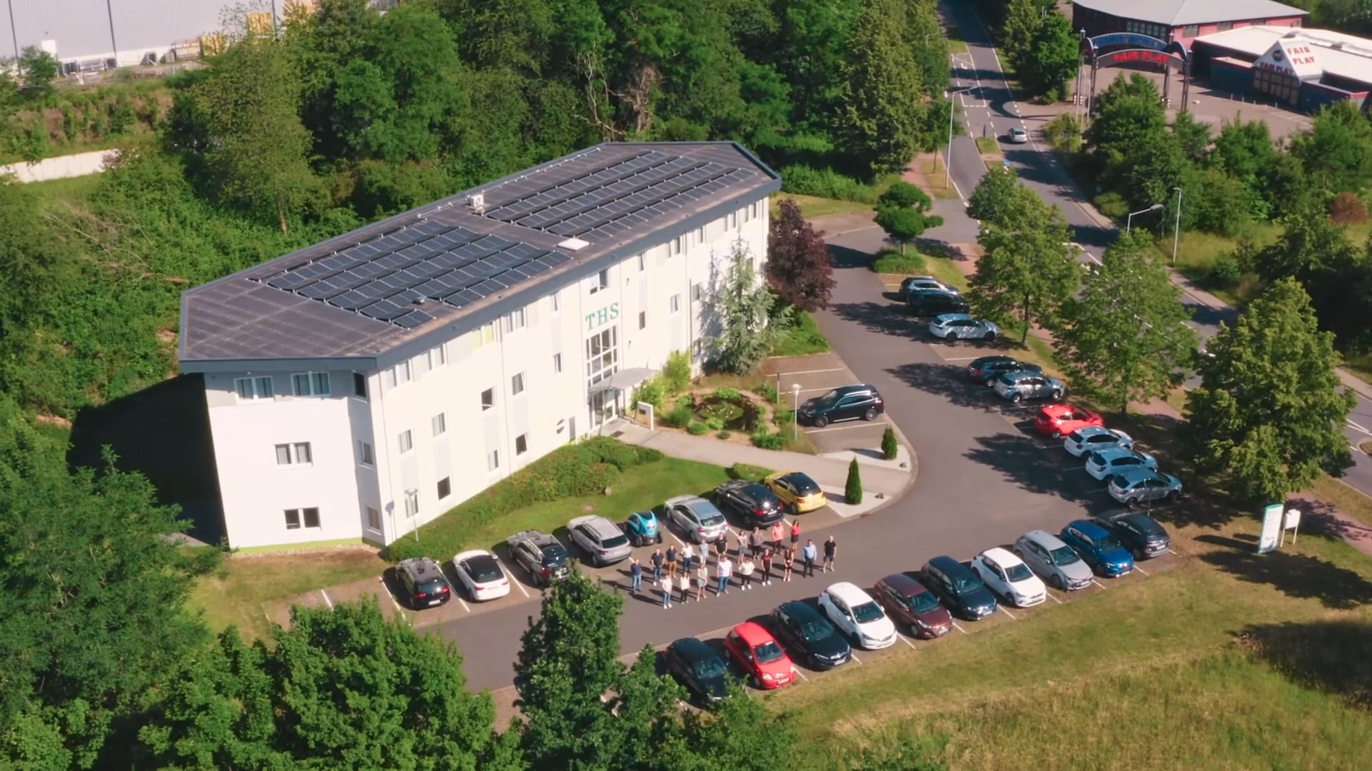 Luftaufnahme eines weißen Bürogebäudes mit Solarpaneelen und einem Parkplatz voller Autos.